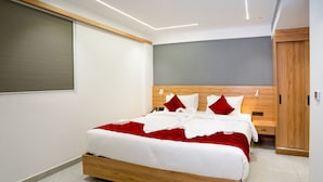 A modern hotel room with a wooden bed, a grey headboard, and a red and white bedspread. - AJ Palace (Ambalapuzha)