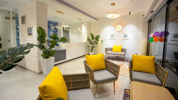 A modern lobby with wicker furniture, yellow cushions, and large windows. - AJ Palace (Ambalapuzha)