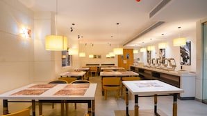 A hotel dining area with tables, chairs, and pendant lighting. - AJ Palace (Ambalapuzha)