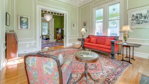 A spacious living room with a red sofa, floral armchairs, a glass coffee table, and a patterned rug.