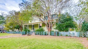 A two-story house with a porch, surrounded by a fence and trees.