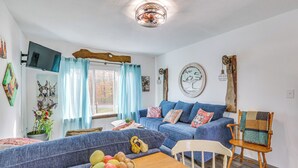 Ein Wohnzimmer mit einem blauen Sofa, einem Holzesstisch mit einer Obstschüssel und einem Holzstuhl.