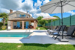 A poolside area with a stone house, lounge chairs, and a large umbrella. - Villa Ida With View (Visnjan)