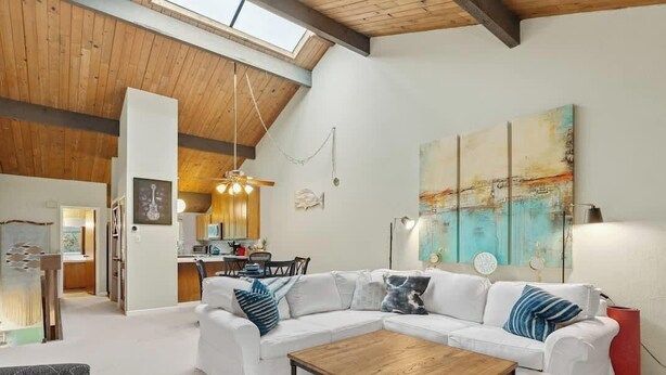 Un salón amplio con un sofá blanco, una mesa de centro de madera y un cuadro abstracto grande en la pared.