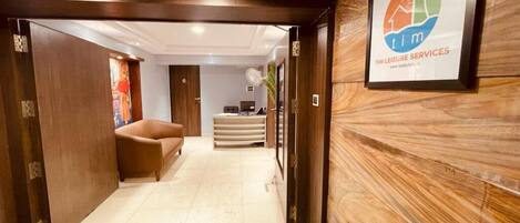 Un área de recepción con pared de madera, mostrador de recepción y una alfombra verde que conduce a una zona de estar.