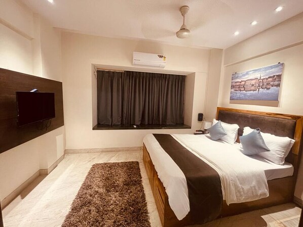 A bedroom with a bed, a window with curtains, a flat-screen TV, and a ceiling fan.