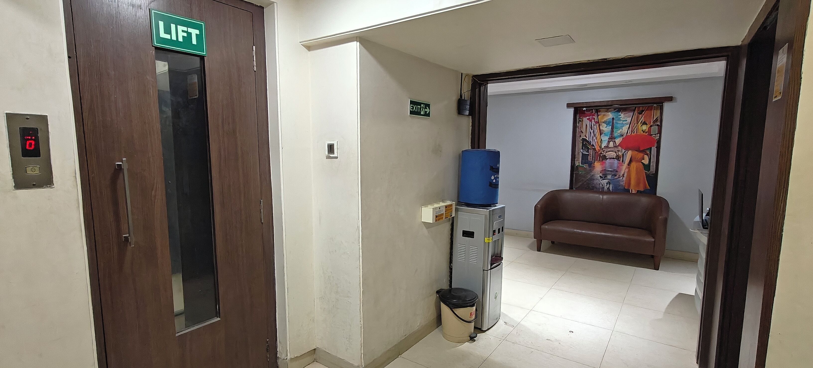 A hallway with a lift, a water dispenser, a trash bin, and a couch.