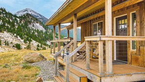 Une cabane en bois dotée d’une terrasse, de grandes fenêtres et surplombant un paysage montagneux.