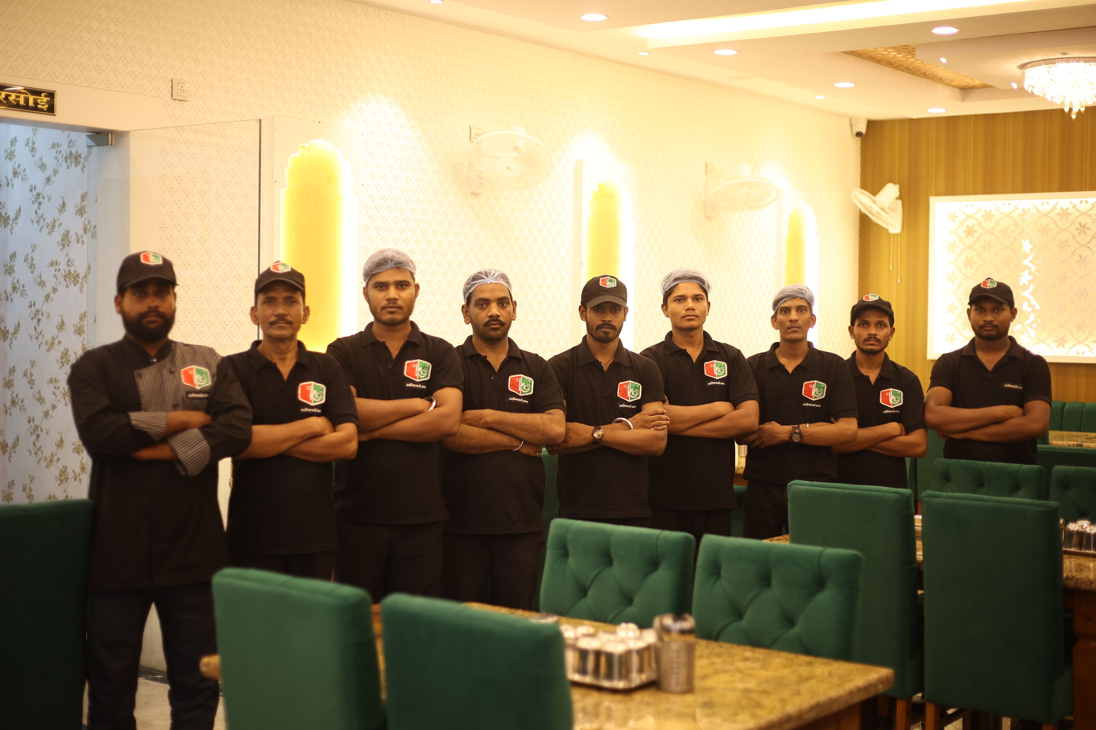A group of men in uniform standing in a restaurant with green upholstered chairs and tables.