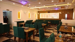 Un restaurant avec des banquettes et des tables recouvertes d’un tissu vert, un sol en marbre et un mur décoratif agrémenté d’un luminaire.