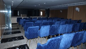 Une salle de conférence avec des rangées de chaises bleues, un sol en marbre et un mur recouvert de panneaux en bois.
