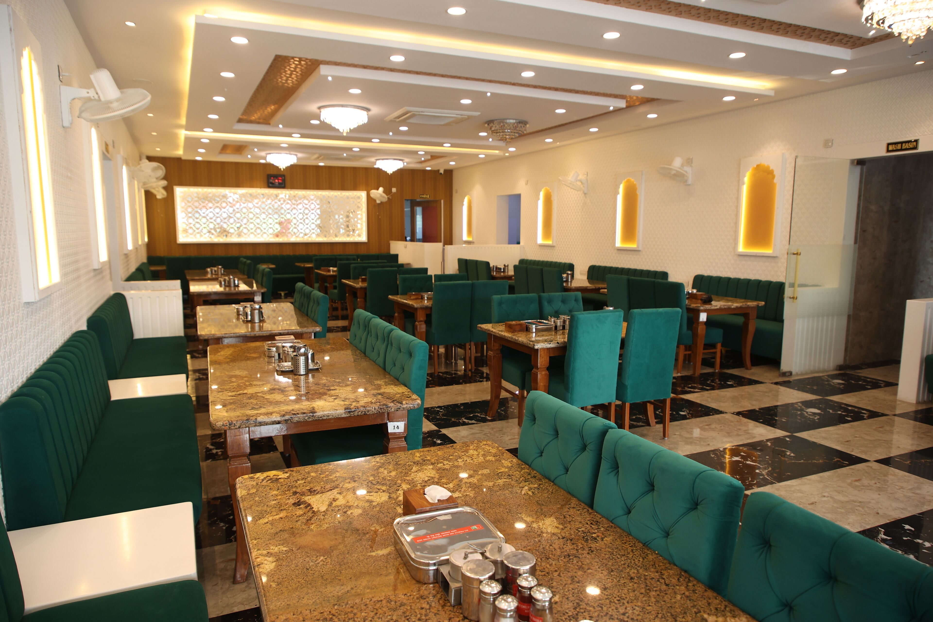 Un restaurant avec des banquettes et des tables vertes, un lustre et un sol à carreaux.