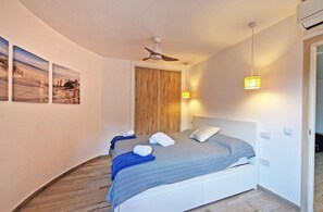 Una camera da letto con un letto, una ventola a soffitto, un'opera d'arte appesa al muro e una lampada da comodino.