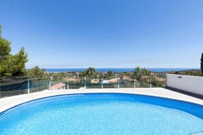 Una piscina limpida e blu con vista sul mare e edifici in lontananza.