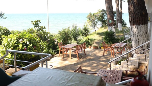 A terrace with wooden furniture, a view of the sea, and a stone wall. - Sahil evim pansiyon (Ünye)