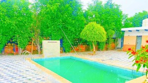 Une piscine dotée d’une terrasse carrelée, entourée d’arbres et d’un bâtiment.