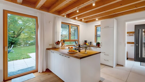 A modern kitchen with a wooden ceiling, large windows, and a view of the garden.