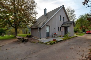 Une maison moderne avec un toit en pente, une cheminée et un petit porche doté de sièges pour l’extérieur.