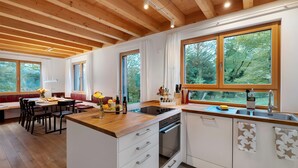 A modern kitchen with wooden beams, large windows, and a dining area with a bench.