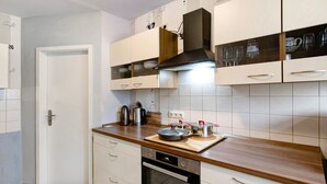 A modern kitchen with white cabinets, a wooden countertop, a built-in oven, and a coffee machine.