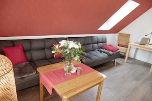Avoin, loft-tyylinen huone, jossa on harmaa sohva, puinen pöytä ja kattovalokuvio.
