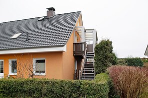 Un immeuble résidentiel doté d’un toit en pente, d’une cheminée visible, d’une fenêtre avec un volet et d’un escalier menant à un étage supérieur.