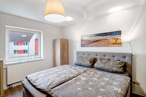 Une chambre à coucher avec un lit, une fenêtre, un radiateur, un tableau et une lampe.