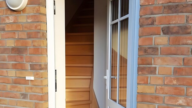 Un bâtiment en briques avec une porte blanche donnant sur un escalier en bois.