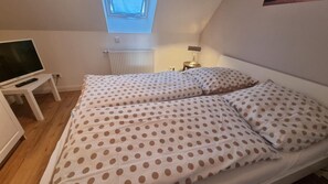A bedroom with a bed, a TV on a stand, a window, and a radiator. - Apartment 'Föhrer Nordseetraum' with Private Terrace, Private Garden and Wi-Fi (Nieblum)