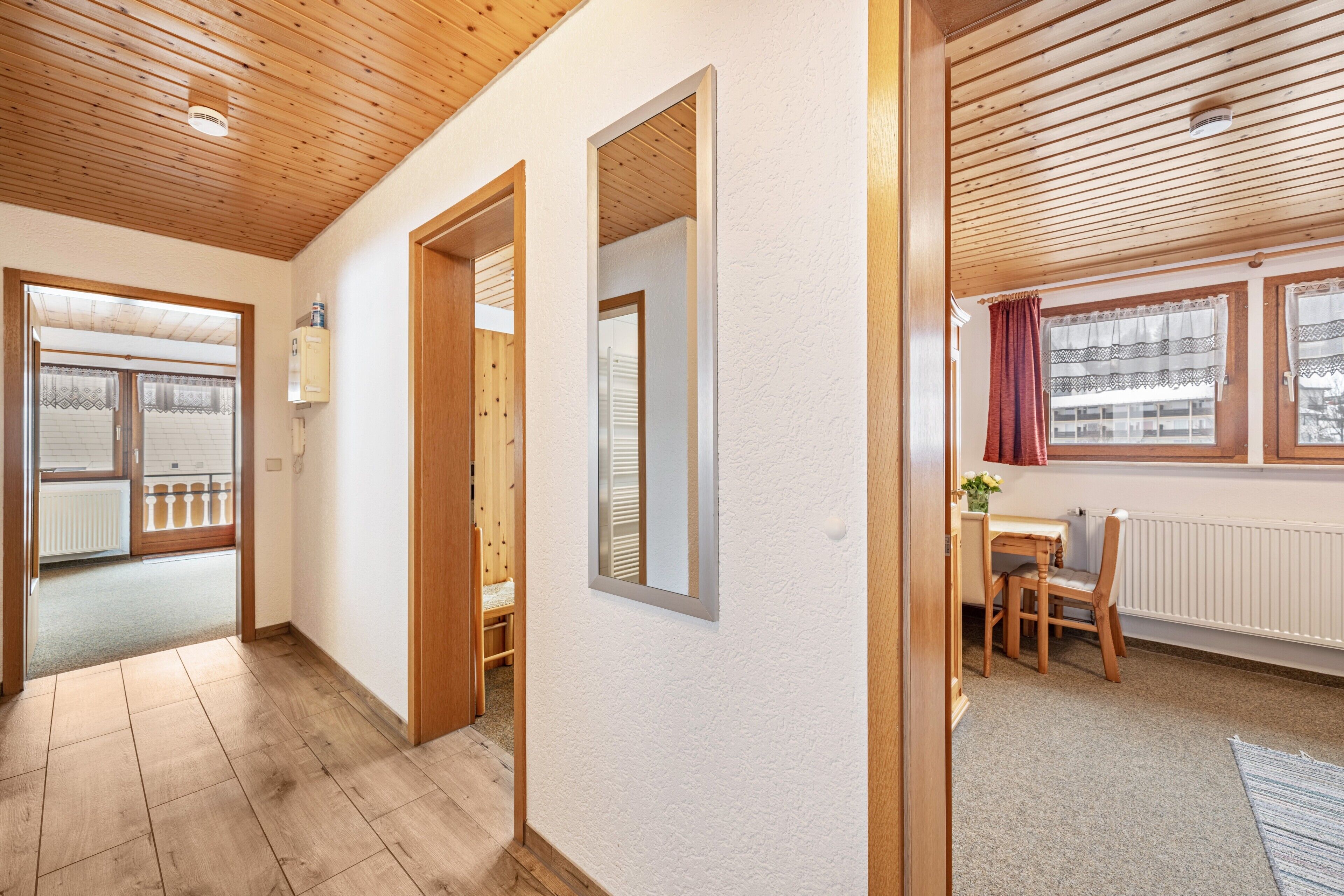 A hallway with wooden flooring, a wooden ceiling, and a view of a balcony with a railing.