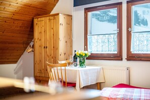 A room with a wooden ceiling, a table with a white tablecloth, a chair, a wooden wardrobe, and a window with a view of a snowy landscape.