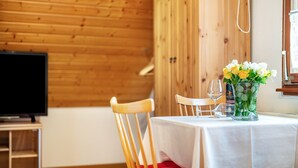 A wooden-paneled room with a television, a table with a white tablecloth, chairs, a vase with flowers, and a wine bottle. - Apartment 'Einzelzimmer' with Mountain View, Shared Terrace and Wi-Fi (Todtnau)