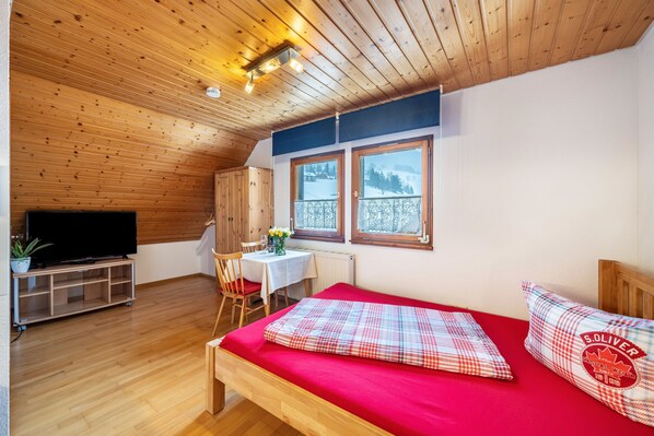 A room with a bed, a TV, a table with chairs, and a window with a view.