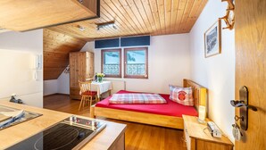 A compact room with a bed, a small table, a chair, a kitchenette, and a window with a view. - Apartment 'Einzelzimmer' with Mountain View, Shared Terrace and Wi-Fi (Todtnau)