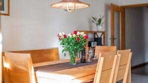 Une table à manger avec des chaises, un vase de fleurs, un verre à vin et une lampe suspendue.