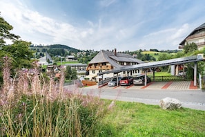Ein Gebäude mit geneigtem Dach, einer überdachten Außenterrasse mit Sitzgelegenheiten und einem Parkplatz mit Autos.