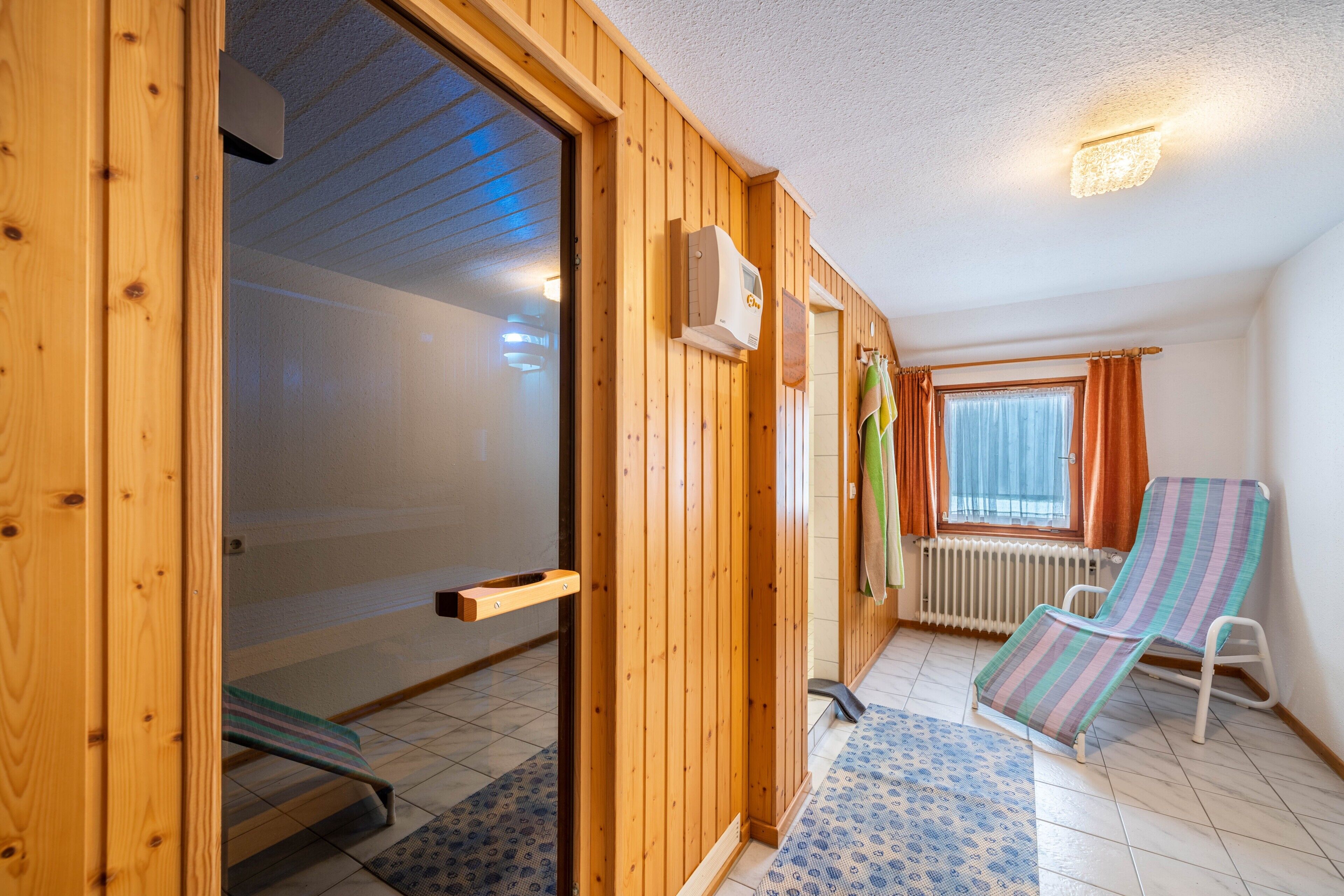 Habitació amb una porta corredissa de fusta, una finestra amb cortines, un radiador i una butaca amb ratlles.