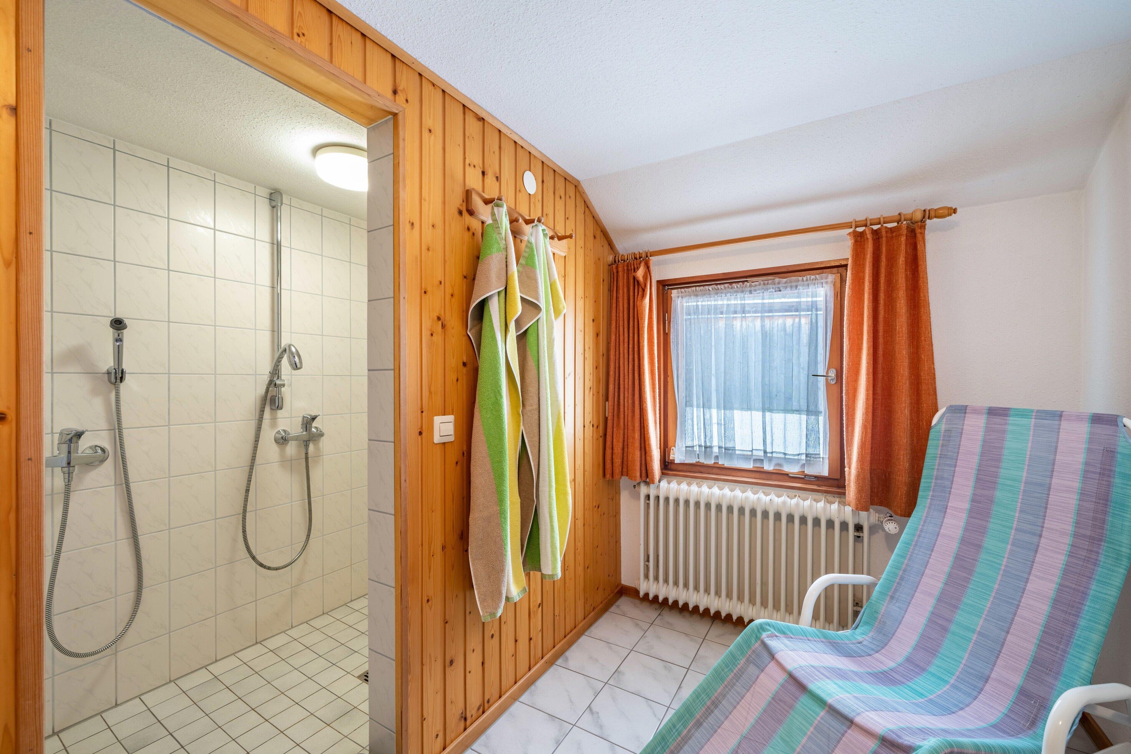 Ein Badezimmer mit Dusche, Handtuchhalter, Heizkörper und einem Fenster mit Vorhängen.