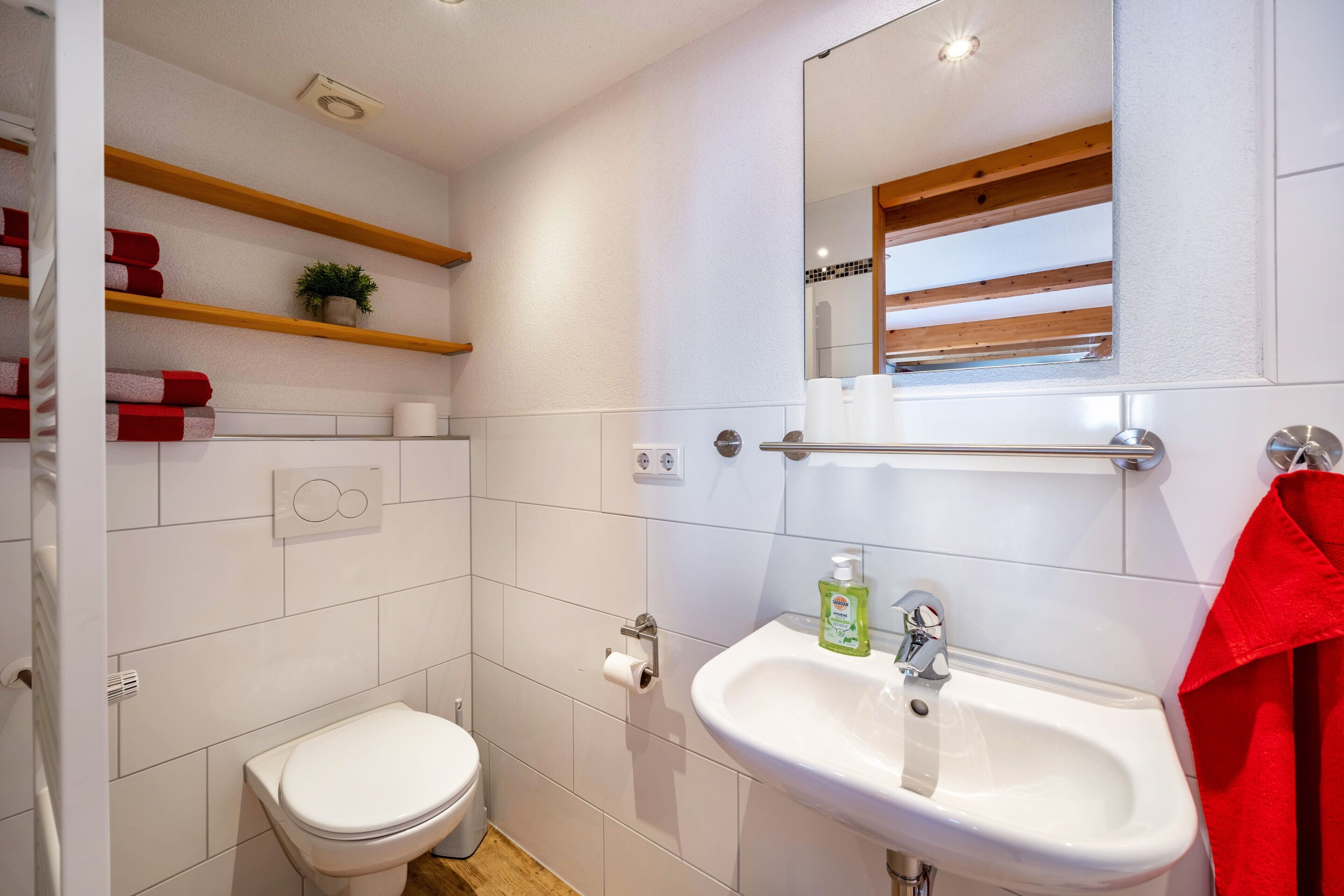 Ein Badezimmer mit Toilette, Waschbecken, Spiegel und Regalen mit Handtüchern.