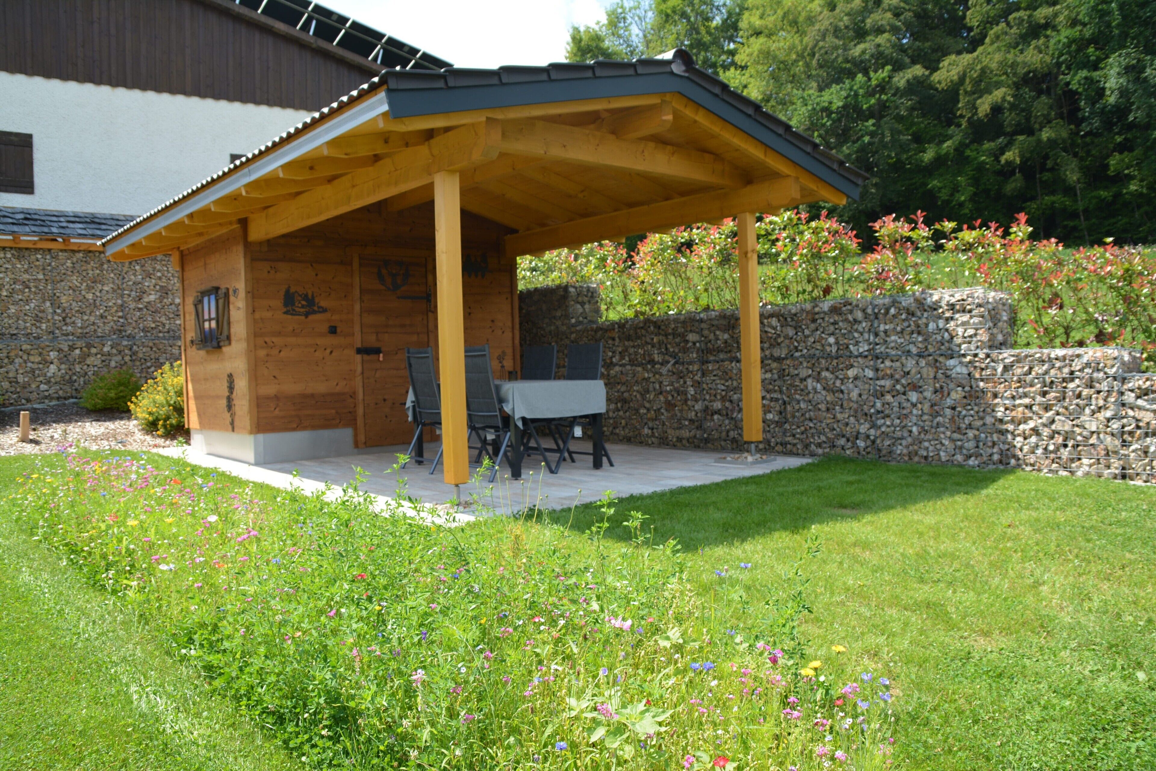 A covered outdoor seating area with a stone wall and a wooden pergola.