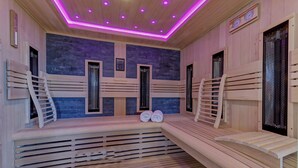 Un sauna avec des bancs en bois, un mur en pierre et un plafond éclairé de lumières violettes.