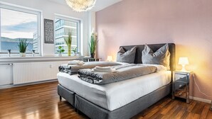 A modern bedroom with a large bed, bedside lamps, a view of the sea, and a radiator.