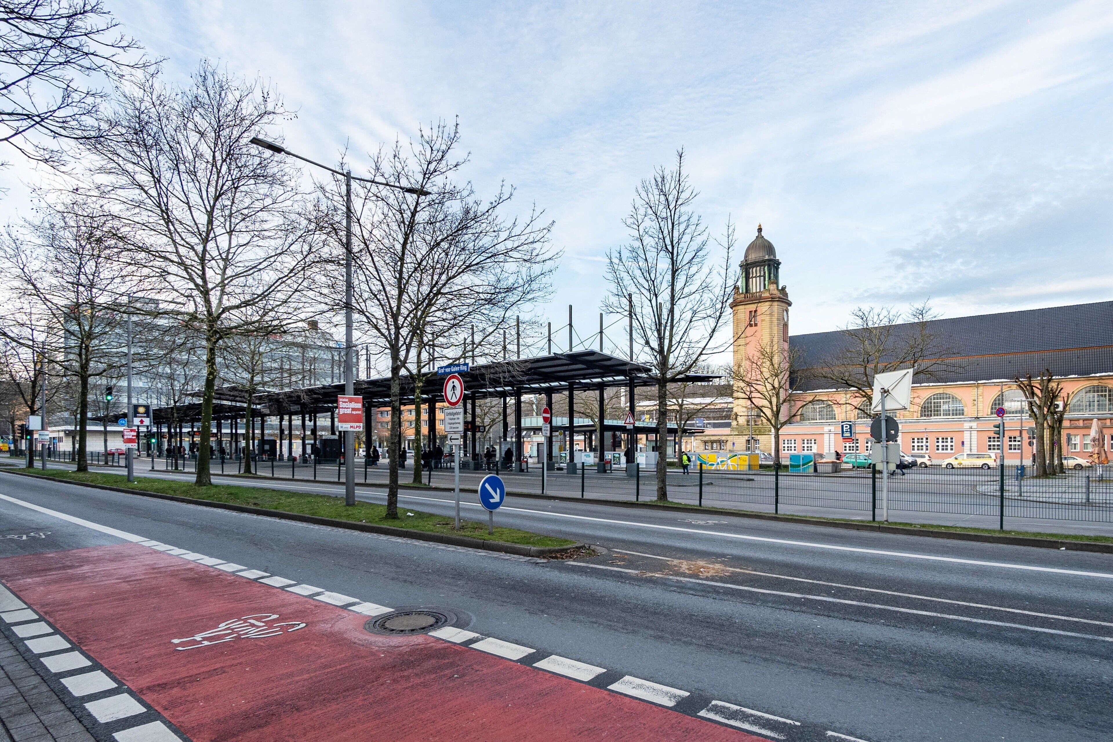 Un arrêt de bus doté d’un abri, une piste cyclable rouge et un bâtiment historique avec une tour en arrière-plan.