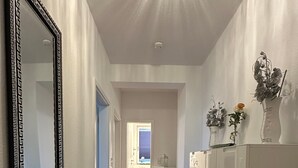 A hallway with a mirror, a bench, a patterned rug, a white cabinet, and a door leading to a bathroom.