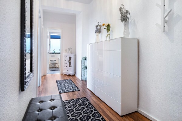 Ein Flur mit einem weißen Kleiderschrank, einer Bank, Teppichen mit Muster und einer Tür zu einem Badezimmer.