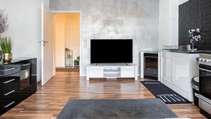 A modern living room with a flat-screen TV, a kitchen area, and a dining space.