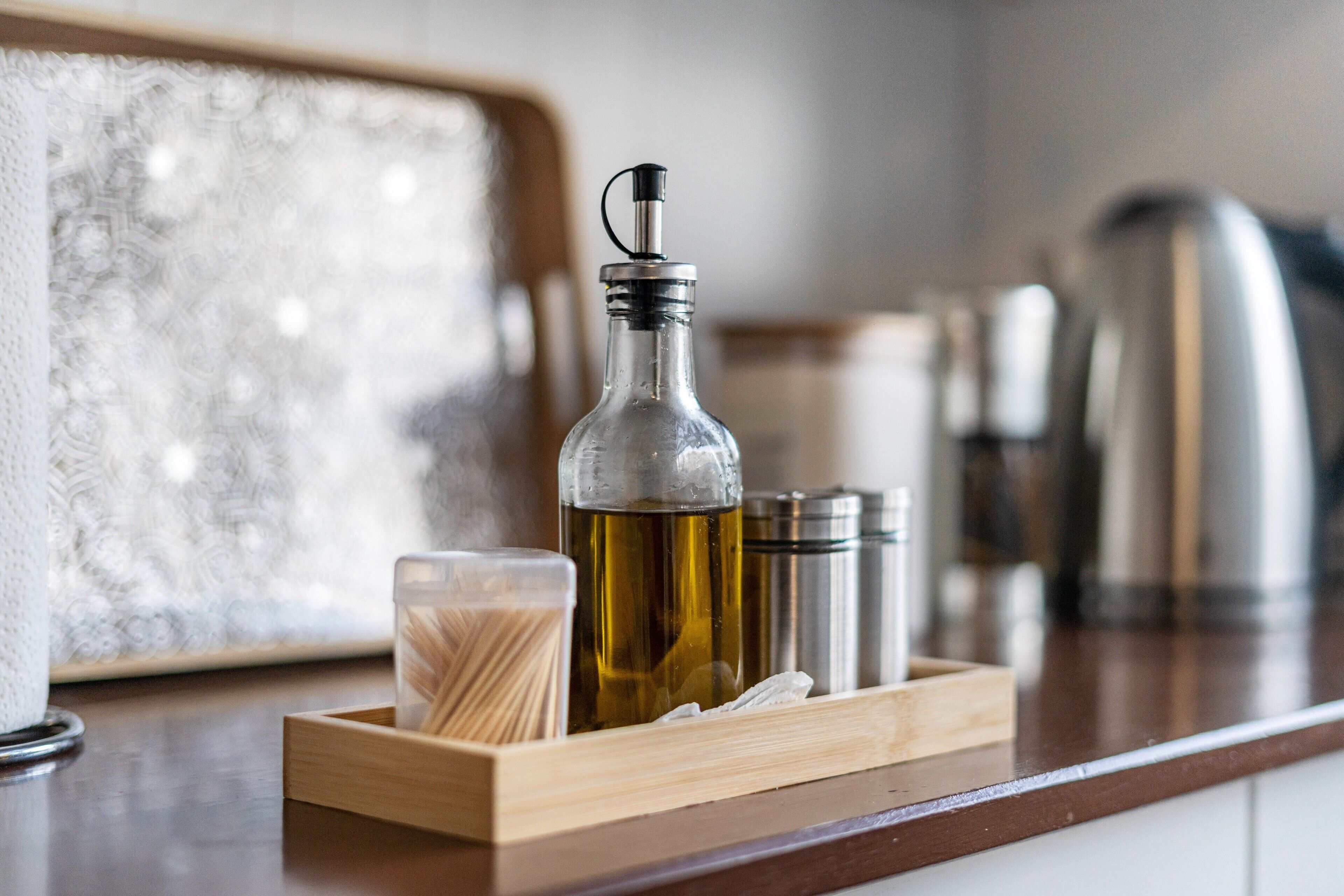 Un comptoir de cuisine sur lequel se trouve un plateau en bois contenant une bouteille en verre, un verre et un récipient rempli d’ustensiles.