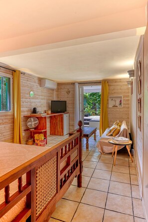 A compact room with a wooden dining table, a small kitchenette with a TV, and a sofa with cushions. - La Case O zoizos (Saint-Joseph)
