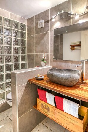 A bathroom with a stone sink, a mirror, and a window with glass blocks. - La Case O zoizos (Saint-Joseph)