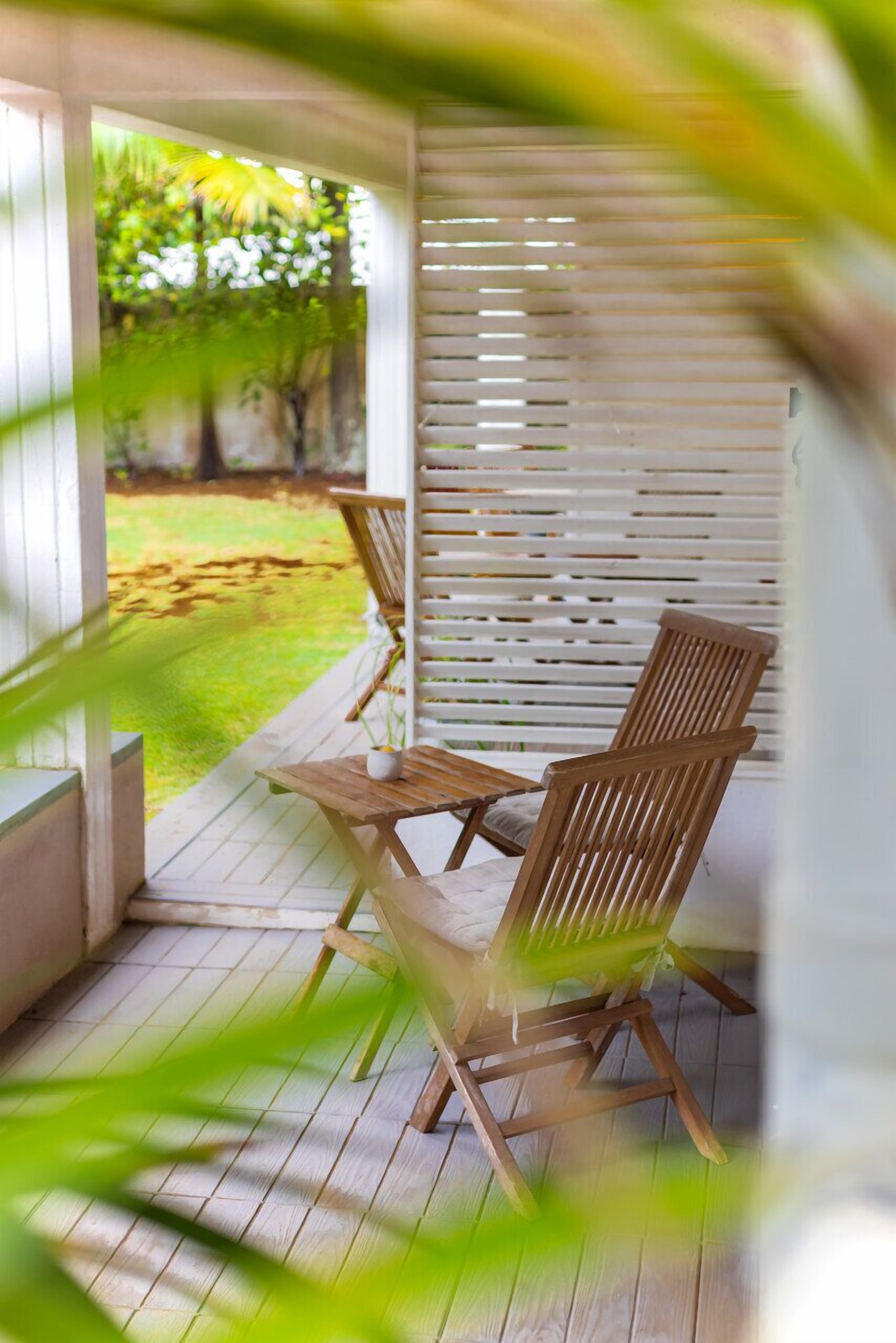 A wooden deck with two chairs and a table, surrounded by white blinds.